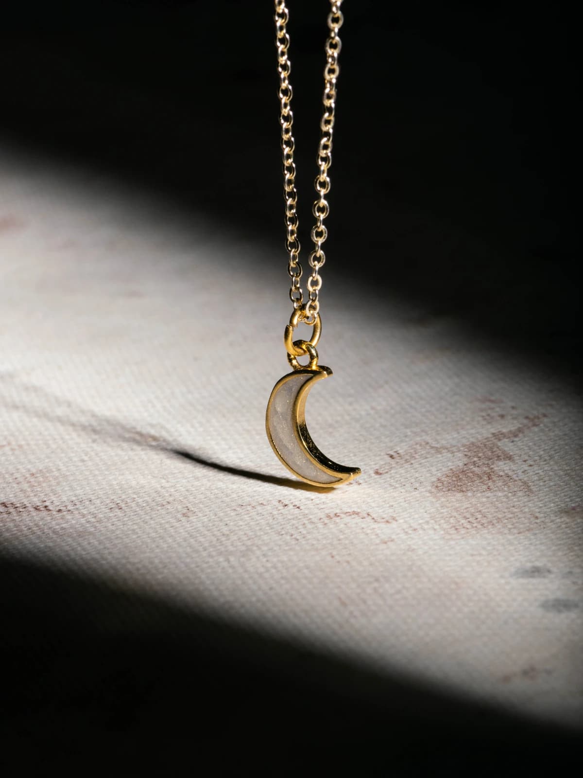 Gold crescent moon pendant necklace on a light fabric backdrop